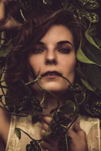 Woman in low light with a pothos around her head and running through her mouth.